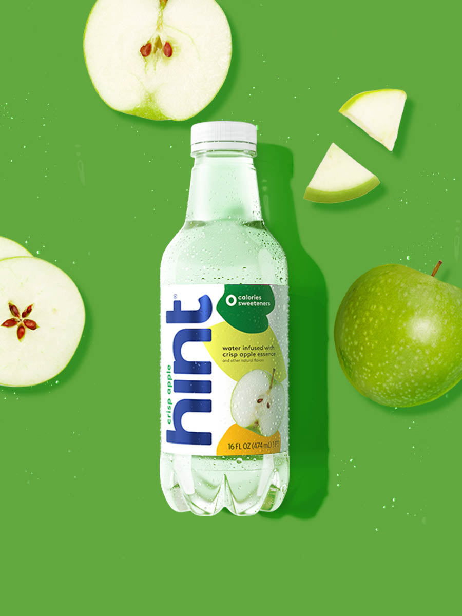 A bottle of Crisp Apple hint water on a vibrant green background. There are various apple pieces alongside the bottle.