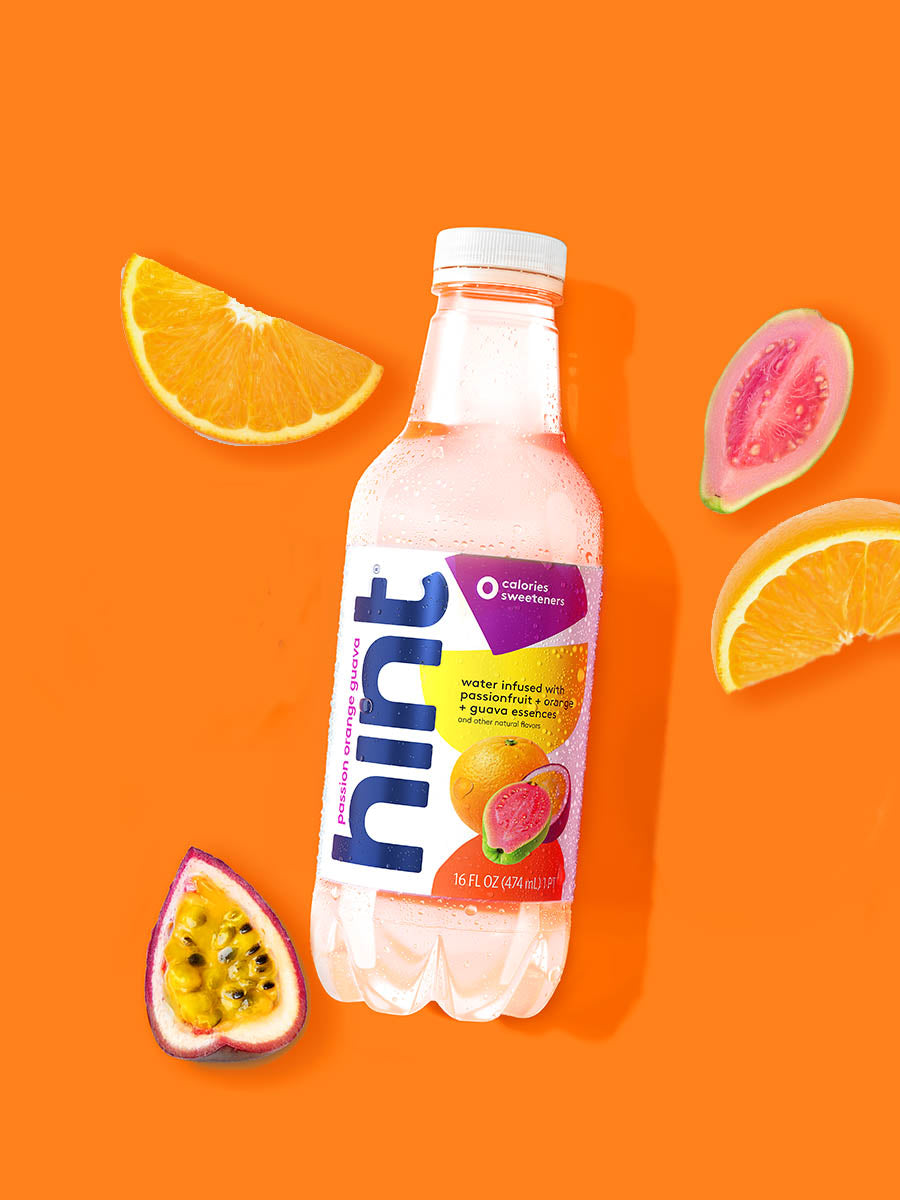 A bottle of Passionfruit, Orange, Guava hint water on an orange background. There are various fruit pieces in the background surrounding the bottle.