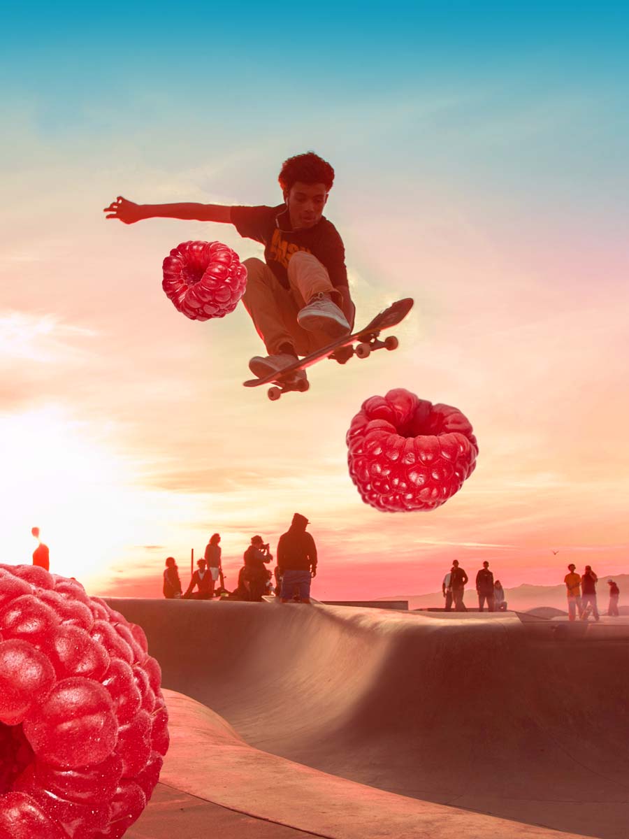 An image of a person jumping in the air with their skate board. There are raspberry fruits in the air with him.