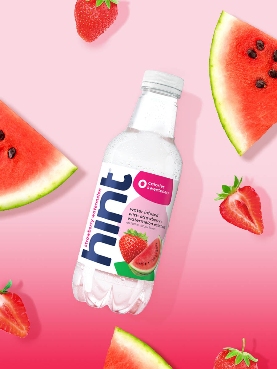 A bottle of Strawberry Watermelon hint water on a pink gradient background. There are various pieces of these fruits alongside the bottle.