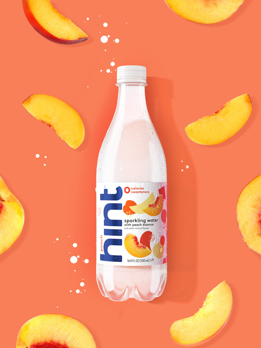 A bottle of peach hint sparkling water on a bright orange background with peach slices in it.