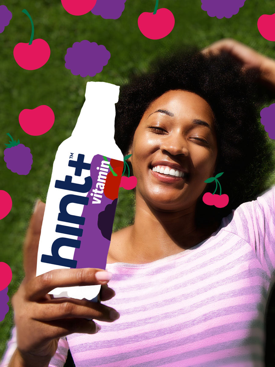 A model laying down holding a graphic of a blackberry cherry hint+ vitamin bottle. There are blackberry cherry graphics overlaying the image.