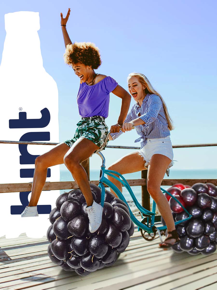 A collage of girls riding a bike on a beach board walk, expect the bike tires are oversized blackberries. There is an oversized bottle of hint water in the background.