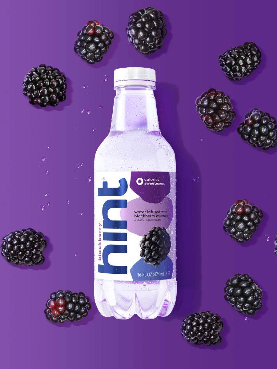 A bottle of Blackberry hint water on a purple background. There are various pieces of fruit in the background. 