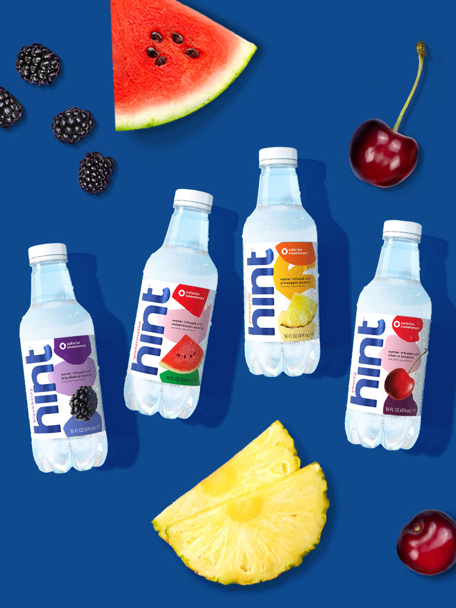 A flatlay photo of 4 hint water flavors on a blue background with various fruit around the bottles.