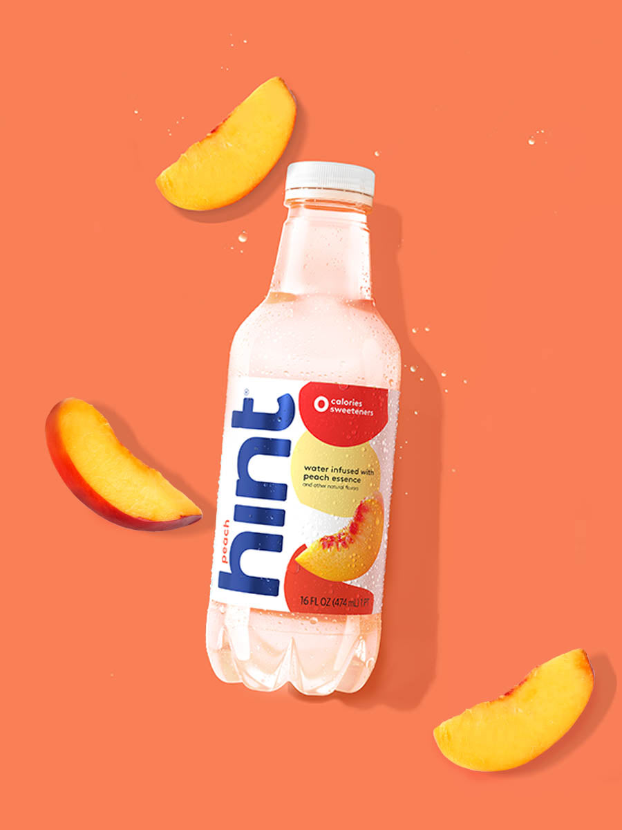 A bottle of Peach hint water on an orange background. There are various peach slices alongside the bottle.