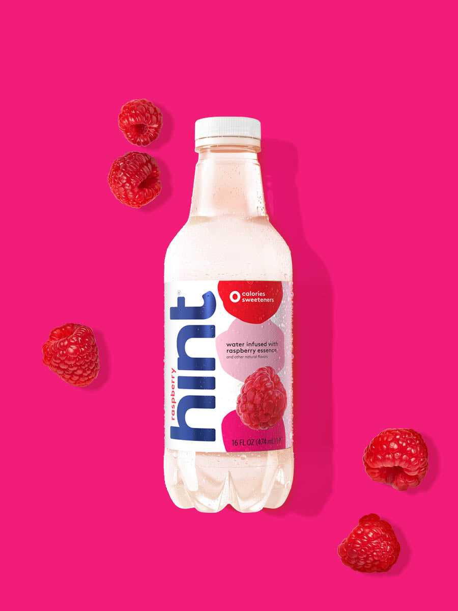 A bottle of Raspberry hint water on a vibrant pink background. There are various raspberries alongside the bottle.