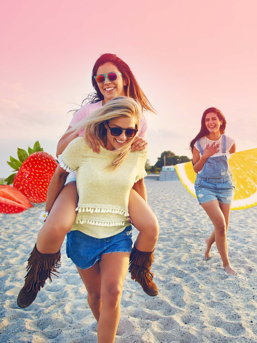 A collage of girls walking on the beach having fun and holding oversized pieces of fruit.