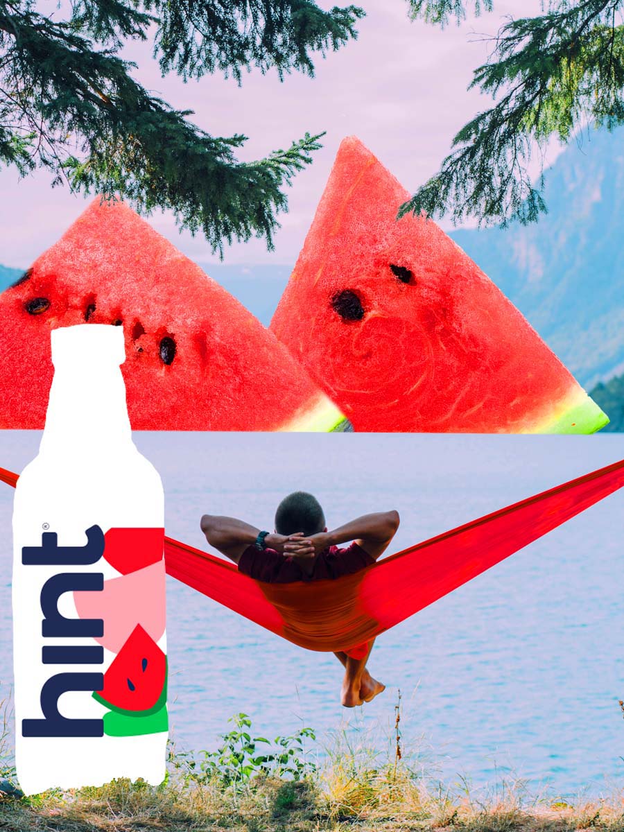 A person laying in a red hammock looking at a lake with watermelon mountains. There is a bottle of hint water in the foreground as a tree.