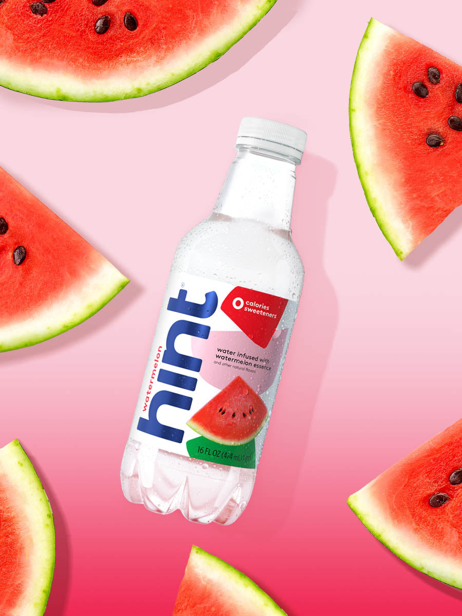 A bottle of Watermelon hint water on a pink gradient background. There are various pieces of fruit in the background. 