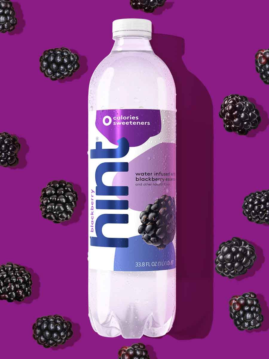 A 1L bottle of blackberry hint water on a red background. There are various blackberry fruit pieces around the bottle.
