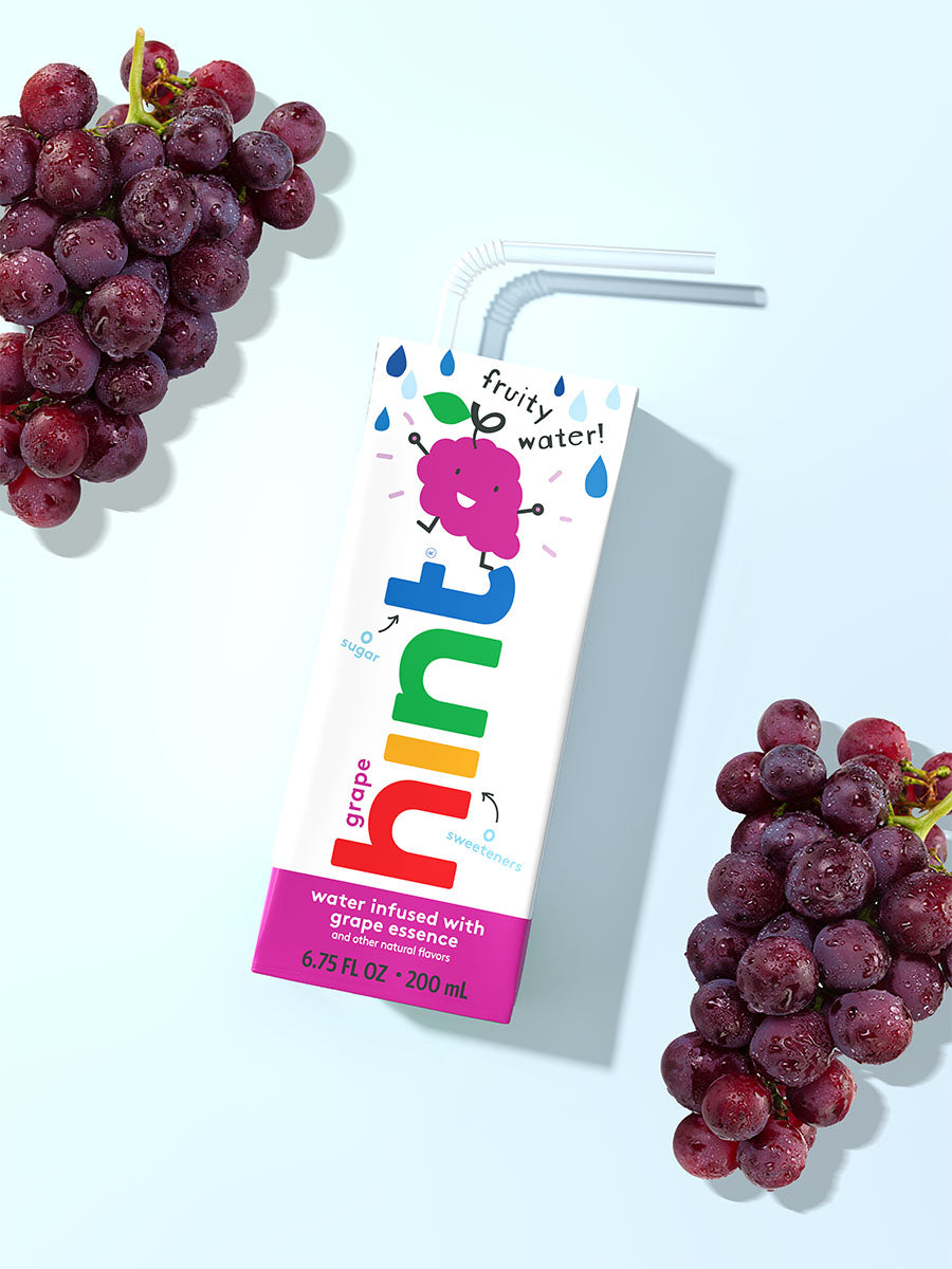 A hint kids water box on a light blue background. It is grape flavored so there are bunches of grape in the photo as well.