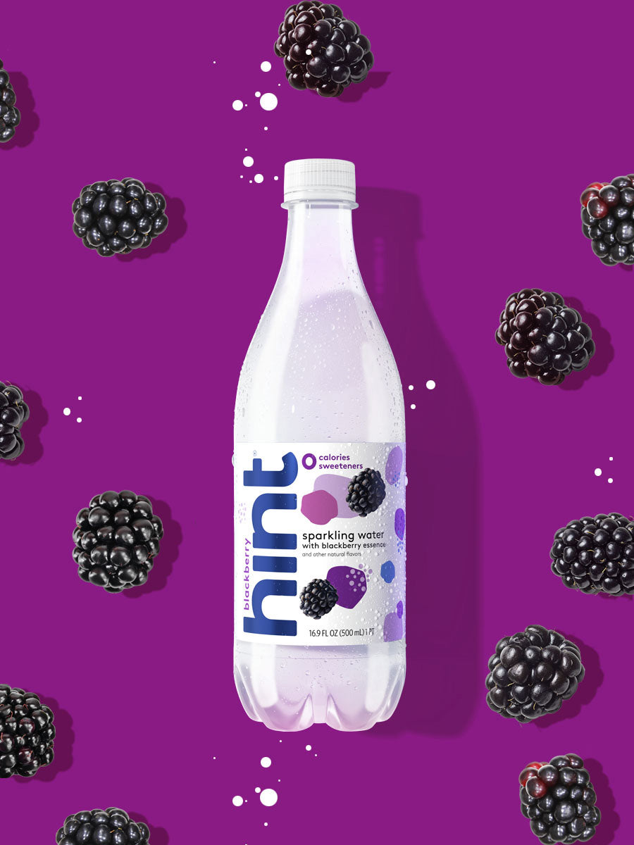 A bottle of blackberry hint sparkling water on a bright purple background with blackberries in it.