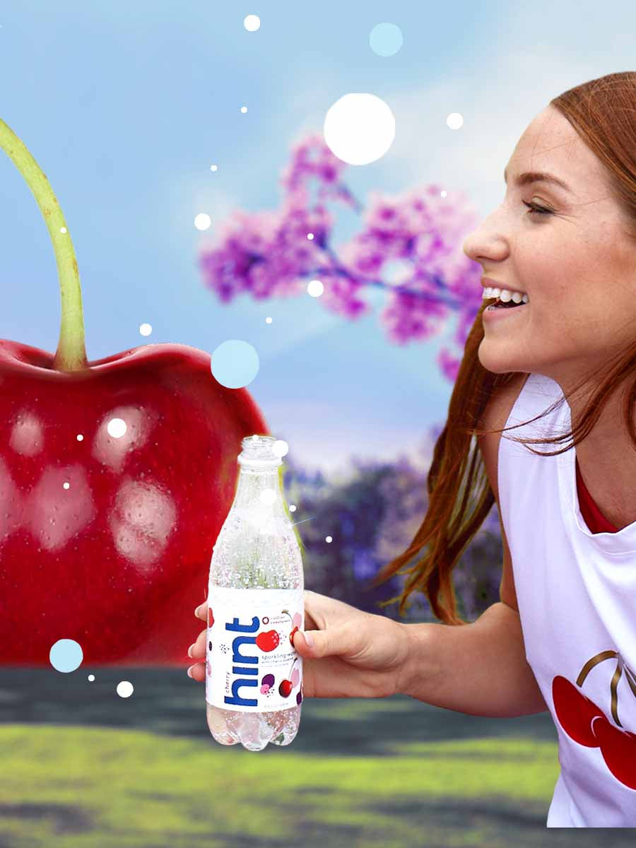 A woman looking left at her bottle of cherry sparkling hint water with a graphic background.