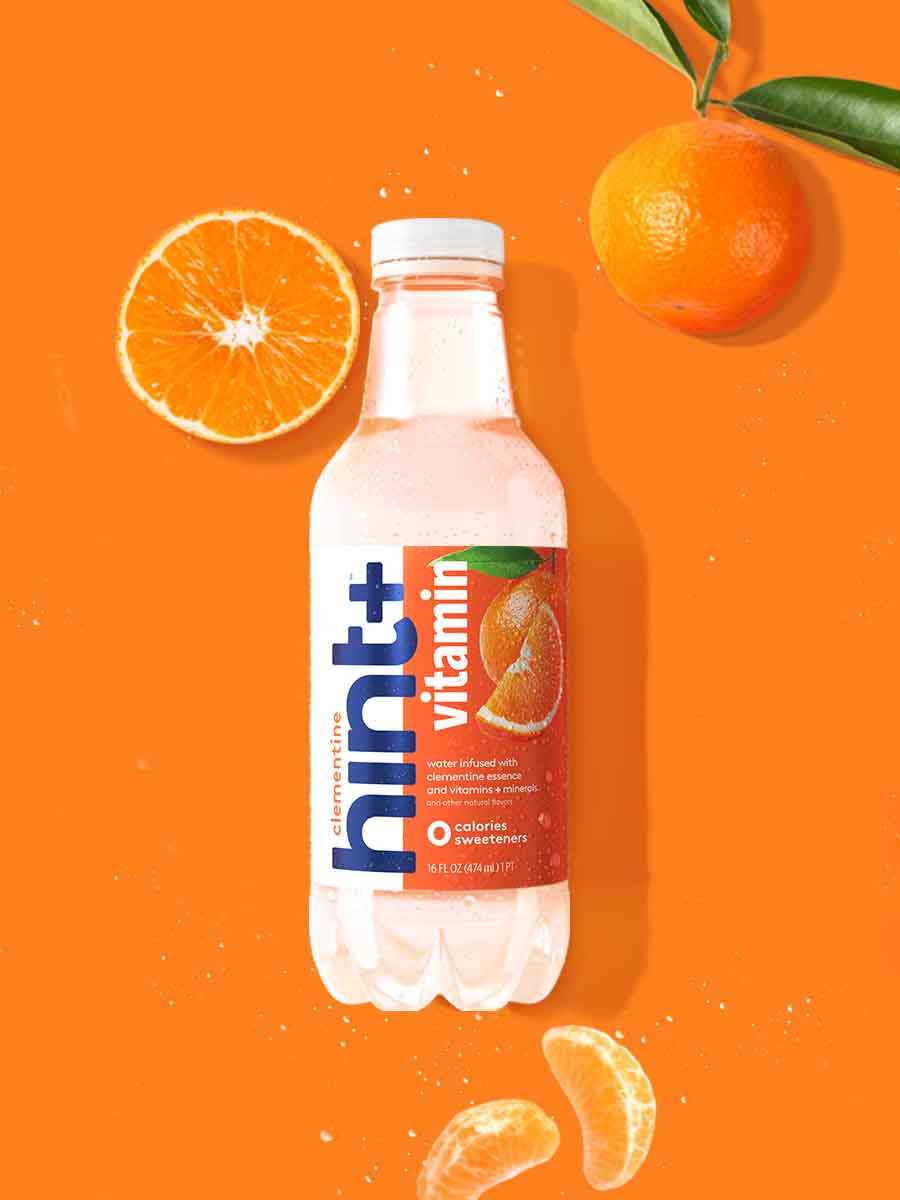 A bottle of clementine hint+ vitamin on an orange background. There are various clementine fruit pieces around the bottle.