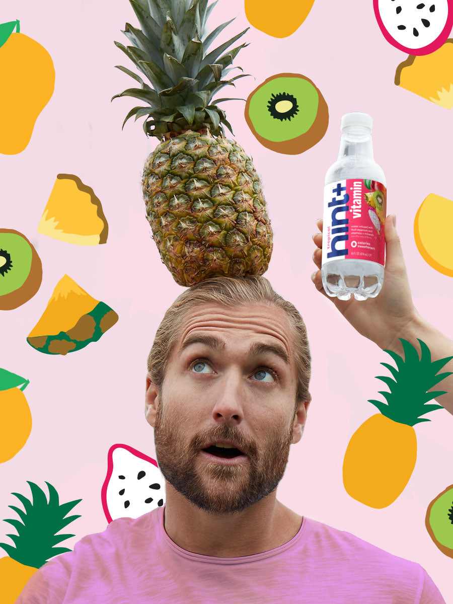 An interesting collage of a man looking up at the pineapple on his head. He is in front of a bright fruit background. There is a hand on the right side holding a bottle of hint+ vitamin.