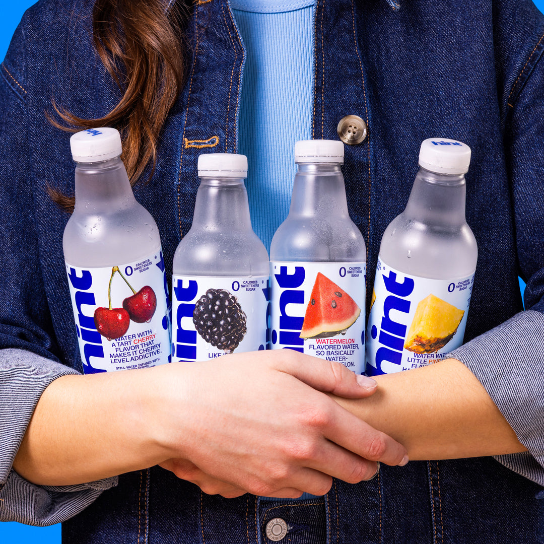 Four Hint flavored water bottles held by crossed arms, flavors tart cherry, blackberry, watermelon, and pineapple