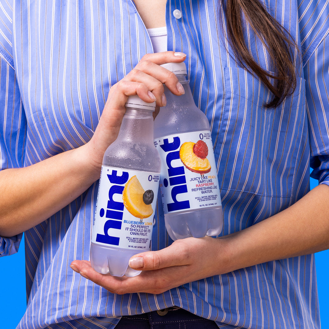 Woman in blue striped shirt holding two bottles of Hint flavored water, blueberry lemon and peach raspberry flavors