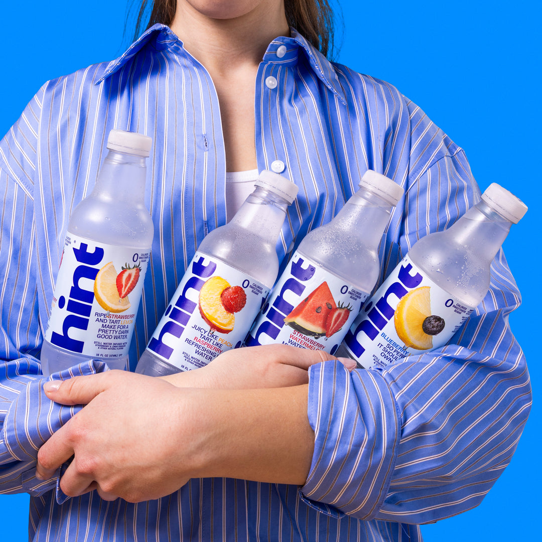 Person in blue striped shirt holding four Hint flavored water bottles: strawberry lemonade, peach raspberry, strawberry watermelon, and blueberry.