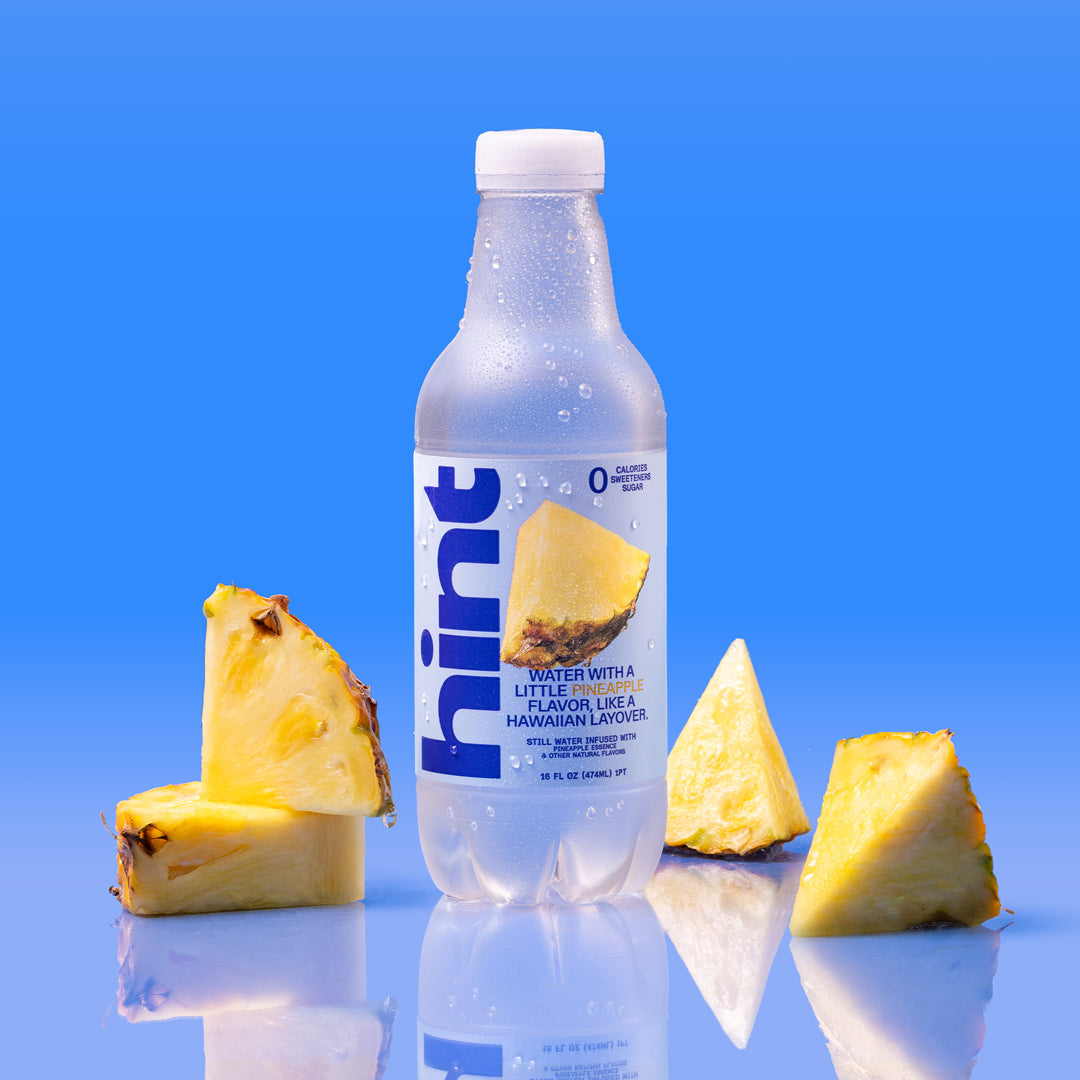 Plastic bottle of Hint pineapple flavored water surrounded by four pineapple slices on blue background
